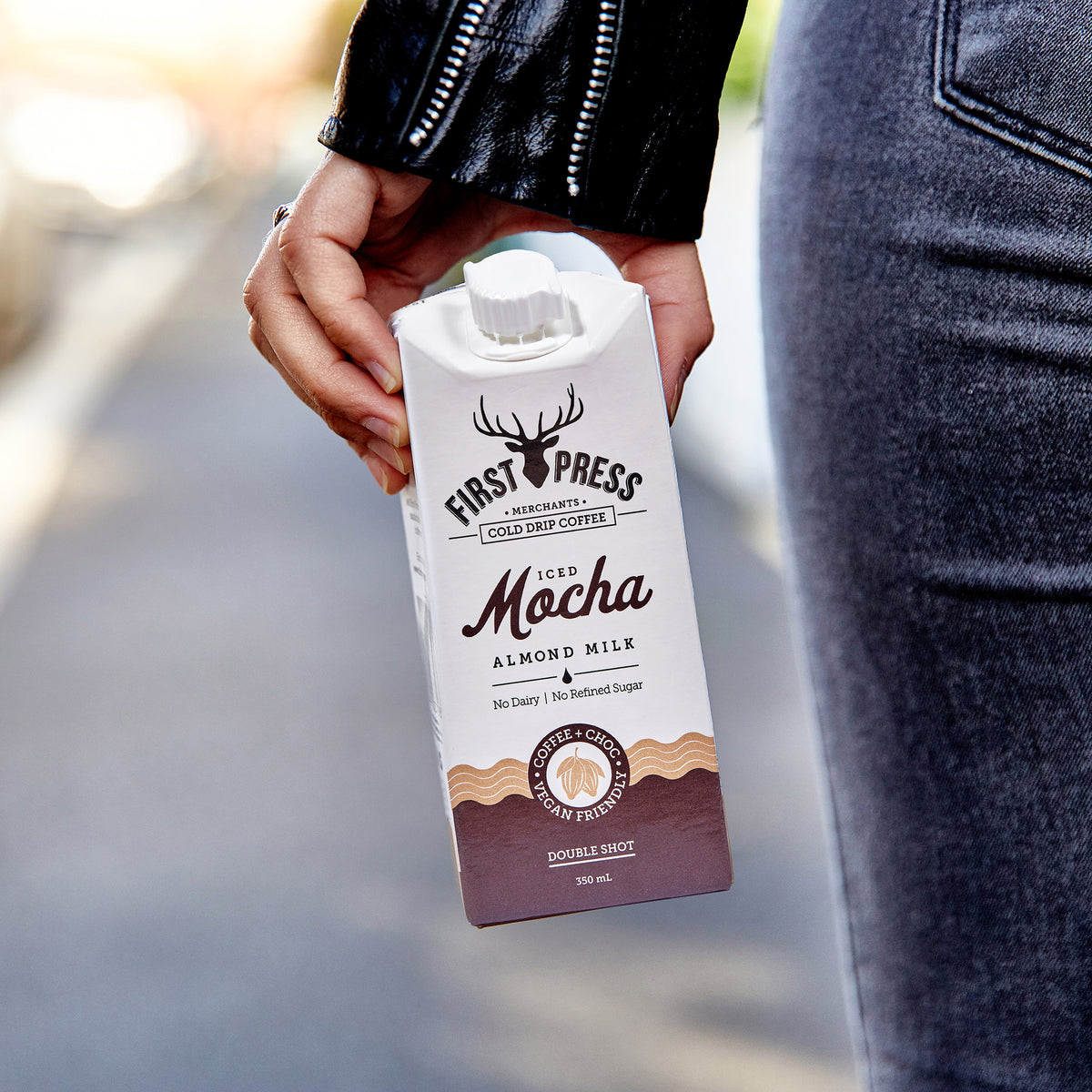 Close up of Iced Mocha Almond Milk, being held next to a person while walking down the street