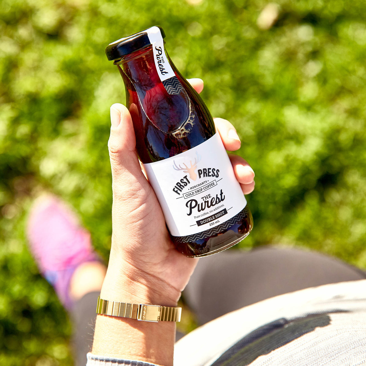 First Press Coffee - The Purest Cold Drip Coffee - 250ml Ready to drink. Person outside holding a bottle of the Purest on the grass